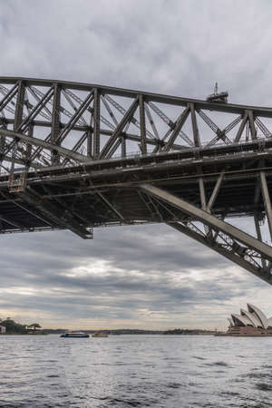 Sydney, Australia - March 22, 2017: Harbour bridge under heavy dark rainy sky seen from under side. Visible under bridge are Opera House, ferry and outlet to ocean.のeditorial素材