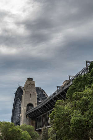 Sydney, Australia - March 22, 2017: Ramp to Harbour Bridge in The Rocks neighborhood under heavy rainy sky. Green trees in front.のeditorial素材