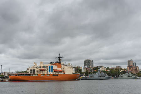 Sydney, Australia - March 23, 2017: Two frigates of the Anzac class and one orange, task unknown, are part of the Royal Australian Navy and docked in the harbor under heavy rainy cloudscape.のeditorial素材