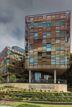 Sydney, Australia - March 25, 2017: Modern colorful facade of University of Sydney Business School with sign under dark heavy sky. green plants up front.のeditorial素材