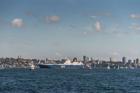 Sydney, Australia - March 26, 2017: Blue white French MN Calao RO-RO Cargo Ship in Sydney harbor on blue water under open sky with residential housing on shore in background.のeditorial素材