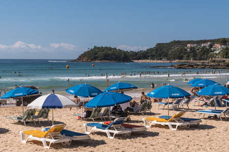 Sydney, Australia - March 26, 2017: Section of Manly Beach with sand and Tasman Sea. Series of beach chairs for hire with blue umbrellas. People on the sand and in the water. Small Shelly beach in distance.のeditorial素材