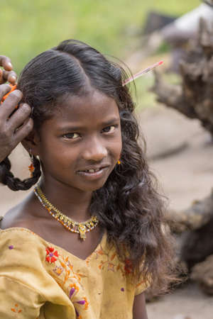 Coorg, India - October 29, 2013: Dubare Elephant Camp. Portrait of Young girl who gets her hair braided. Wears yellow dress, golden earrings and necklace. Green background.のeditorial素材