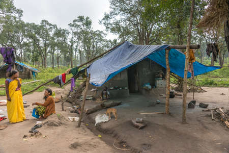 Coorg, India - October 29, 2013: Dubare Elephant Camp. Family scene with mother, daughter and old grandfather in front of dirt hut with blue tarp . Forest background. Dog, tools and laundry.のeditorial素材