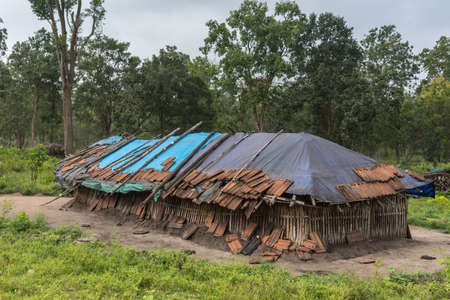 Coorg, India - October 29, 2013: Dubare Elephant Camp. Family dwelling is long bamboo-clay hut with blue tarp and some panes as roof. Green jungle setting under gray sky.のeditorial素材