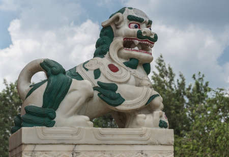 Coorg, India - October 29, 2013: The guardian statue of the mutached snow lion on the step of the Padmasambhanva Vihara of Namdroling Buddhist Monastery, Some green trees in back. Blue sky with cloudscape.のeditorial素材