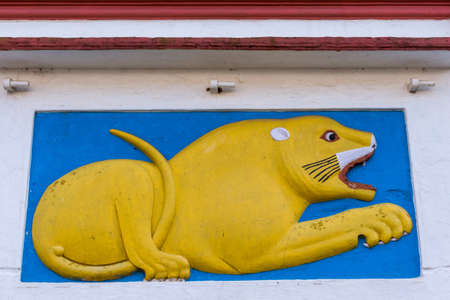 Madikeri, India - October 31, 2013: Shree Omkareshwara Temple. Mural of yellow lying male lion on white extermal wall. Set in sky-blue square under marron roof edge.のeditorial素材