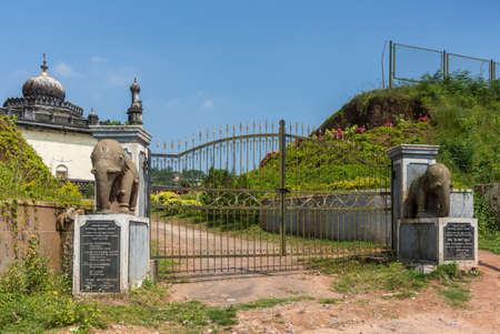 Madikeri, India - October 31, 2013: Entrance gate with elephant statues to the mausoleum domain for the Haleri kings, the Raja Tombs. Blue sky and green vegetation. Dirt road. Blue Sky.のeditorial素材