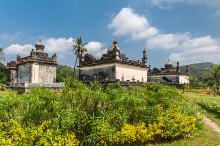 Madikeri, India - October 31, 2013: Three largest white and gray Royal mausolea set in green garden of domain Raja Tombs under blue sky with clouds. Bushes and trees.のeditorial素材
