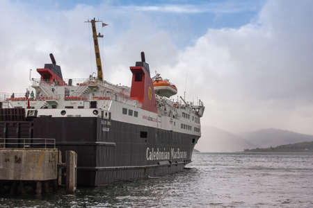 Ullapool, Scotland - June 8, 2012: Black white and red ferry boat named Caledonian Macbrayne docked in harbor of Ullapool on Loch Broom. Fog over water, hills and cloudscape in back.のeditorial素材
