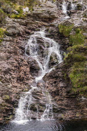 Braemore, Scotland - June 8, 2012: Closeup of Dundonnell Rvier rapids along A832 road offers bronwn rocks and grassy hills under dark cloudscape. Hills in back. Brown pool in front.のeditorial素材