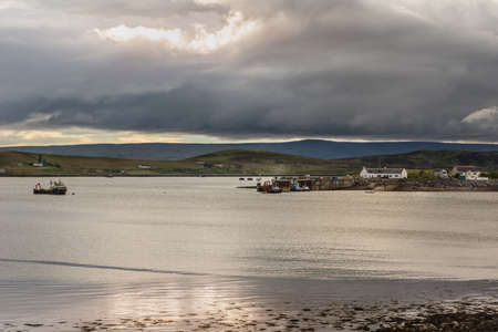 Aultbea, Scotland - June 8, 2012: Calm waters of Loch Ewe with the pier and harbor of Aultbea under dark rainy cloudscape. Fishing vessel. Green hills in background.のeditorial素材