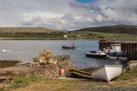 Aultbea, Scotland - June 9, 2012: Harbor of Aultbea with pier and a few sloops and fishing vessels. Lobster traps on shore. Forested hills in back. Gray and white cloudscape.のeditorial素材
