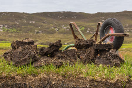 Inverasdale, Scotland - June 9, 2012: Closeup of turned over rusty wheel barrel at peat digging site. Green grass as background.の写真素材