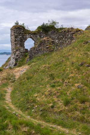 Stromeferry, Scotland - June 10, 2012: Path leading up green hill to Window in rock wall of Castle Strome ruins at Loch Carron.  Mountains on horizon.のeditorial素材