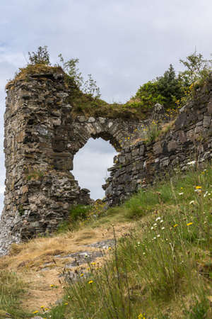 Stromeferry, Scotland - June 10, 2012: Closeup of Window in rock wall of Castle Strome ruins on green hill. Yellow and green weeds up front.のeditorial素材