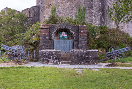 Dornie, Scotland - June 10, 2012: Historic artillery pieces with WW1 war memorial outside wall of Eilean Donan Castle. Emblems and list of in Flanders fallen soldiers. Green vegetation up front.のeditorial素材