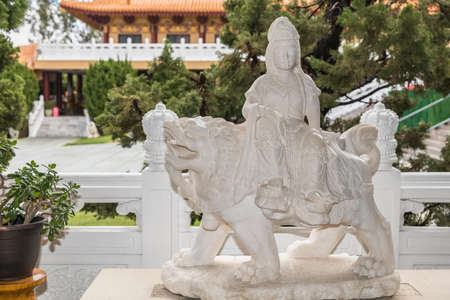 Hacienda Heights, CA, USA - March 23, 2018:  White statue of Avalokitesvara Bothisattva, Guanyin, holding prayer beads and sitting on lion on side of garden at Hsi Lai Buddhist Temple.のeditorial素材