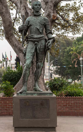 Los Angeles, CA, USA - April 5, 2018: Green Bronze statue of Spanish King Carlos III, ordered the founding of El Pueble Los Angeles, shows slender middle-aged man. Back is gray tree trunk, some flags and silver sky.のeditorial素材