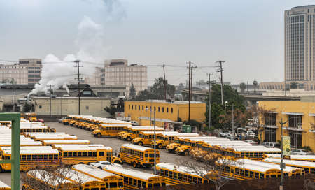 Los Angeles, CA, USA - April 5, 2018: Part of large school bus parking lot on corner of Alameda and College streets under gray sky. Yellow buildings and smoke plume.のeditorial素材