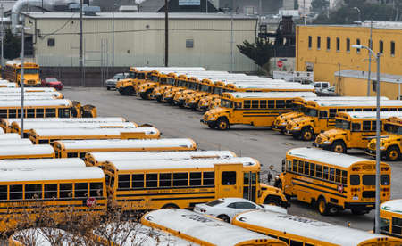 Los Angeles, CA, USA - April 5, 2018: Part of large school bus parking lot on corner of Alameda and College streets under gray sky. Yellow buildings.のeditorial素材