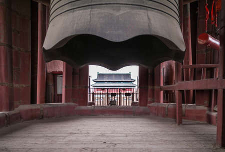 Beijing, China - April 26, 2010: Closeup of giant gray metal bell hanging from massive red support bridge in historic Bell Tower. Look through building  under bell and see Drum Tower.のeditorial素材
