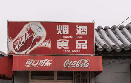 Beijing, China - April 26, 2010: Closeup of red Coca-Cola sign fixed on gray roof against silver sky. Read in English and Mandarin about beer, cigarette and food.のeditorial素材