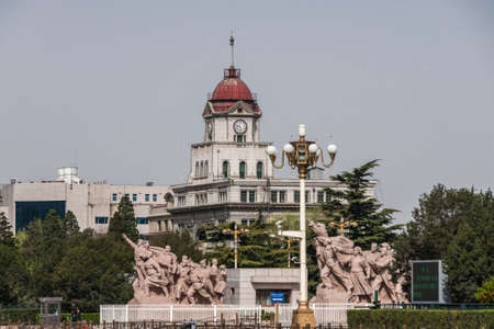 Beijing, China - April 27, 2010: Gray with red dome roof building is former railway station with clock tower at Tienanmen Square, Part of the Monument to the Peopleâs Heroes in front. Green trees.のeditorial素材