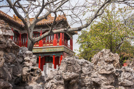Beijing, China - April 27, 2010: Forbidden City. Red-pillared second-level apartment of private quarters peeps above gray rocks and between flowering trees under light blue sky.のeditorial素材