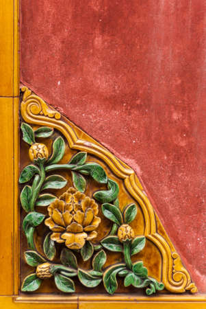 Forbidden City. Closeup of flowerly corner ceramic tile decoration of a red wall shows yeillow flowers with green foliage. Lower Left corner.の写真素材
