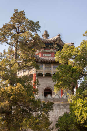 Beijing, China - April 29, 2010: Summer Palace. Closeup of gray-red-blue pagoda style tower captured between green trees under light blue sky.のeditorial素材