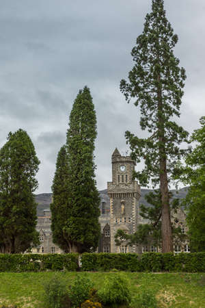 Fort Augustus, Scotland - June 11, 2012: The clock tower of Abbey Highland Club, seen between trees, fronted by garden under heavy cloudscape. Hills on horizon.のeditorial素材