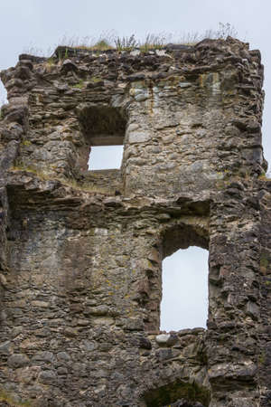 Invergarry, Scotland - June 11, 2012: Closeup of Tall dark-brown ruined wall with window openings of castle Invergarry, under gray sky.のeditorial素材