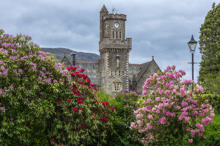 Fort Augustus, Scotland - June 11, 2012: Closeup of the Abbey Highland Club clock tower with flowers fronted by garden  under heavy cloudscape.のeditorial素材