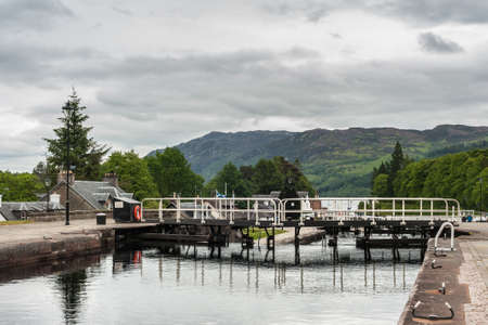 Fort Augustus, Scotland - June 11, 2012: Lock filled with water to the point of overflowing. Walkway over lock doors. Green Hills on horizon. All under heavy cloudy sky.のeditorial素材