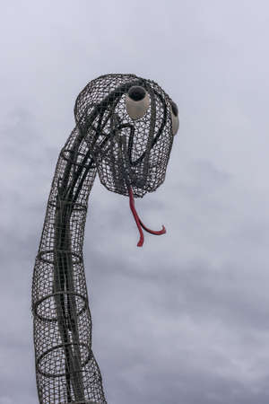 Fort Augustus, Scotland - June 11, 2012: Art made of chicken wire. Closeup of giant head of Nessie the Loch Ness Monster against gray sky. Red tongue. Along Locks on Oich Canal.のeditorial素材