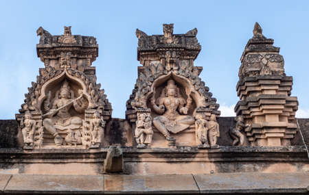 Shravanabelagola, Karnataka, India - November 1, 2013: Brown stone with black mold statues in niches on edge of roof at Jain Tirth building shows also small scene of love making and others under blue sky.のeditorial素材