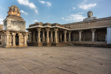 Shravanabelagola, Karnataka, India - November 1, 2013: Courtyard with tempe structures on pillars. Head of giant Bhagwan Bahubali peeps over them under blue sky with white clouds.のeditorial素材
