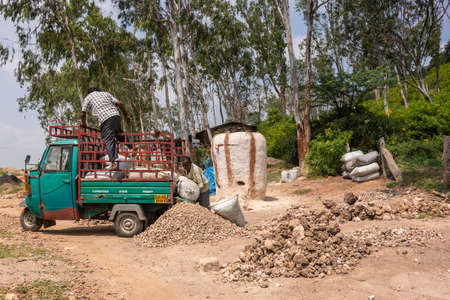 Hunsur, Karnataka, India - November 1, 2013: Two men Load white bags of lime onto light green truck....