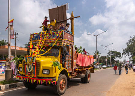 Mellahalli, Karnataka, India - November 1, 2013: Karnataka Rajyotsava Parade. A yellow dump truck loaded with children closes the parade. Flags and flowers Street scene with cars and people.のeditorial素材