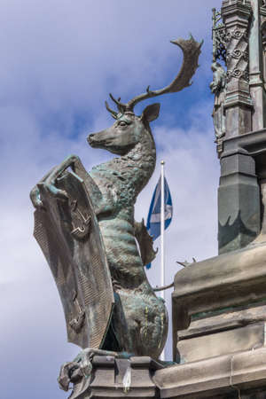 Edinburgh, Scotland, UK - June 14, 2012; Deer holding shield on Statue pedestal of Walter Montagu Douglas Scott, Duke of Buccleuch on Parliament Square. Against blue sky and Scottish flag.のeditorial素材