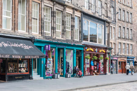 Edinburgh, Scotland, UK - June 14, 2012: Colorful facades of several shops in a row on Royal Mile as street level of tall historic brown houses. Whisky, souvenirs, clothes, cigars, and more.のeditorial素材