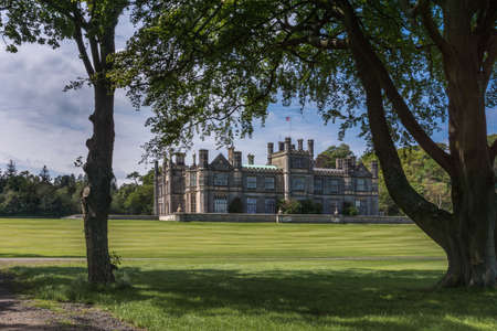 Edinburgh, Scotland, UK - June 14, 2012: Dalmany house, mansion and castle in Tudor revival style as seen from under foliage of woods. Blue sky.のeditorial素材