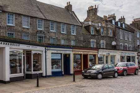Queensferry, Scotland, UK - June 14, 2012: Small shops in the shopping High Street. shops painted frames. Upstairs, brown stone. Cars and gray street surface. Cloudscape.のeditorial素材