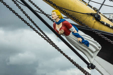 Glasgow, Scotland, UK - June 17, 2012: Closeup of figurehead representing blonde woman with gray dress, maroon vest and blue scarf, on the bow of Tall ship docked at Riverside Museum. Heavy black cables and yellow bow beam.のeditorial素材