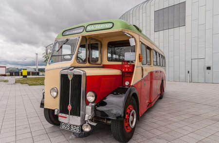 Glasgow, Scotland, UK - June 17, 2012: Along River Clyde, outside Riverside Museum antique red, green and yellow passengers bus under heavy cloudscape.のeditorial素材