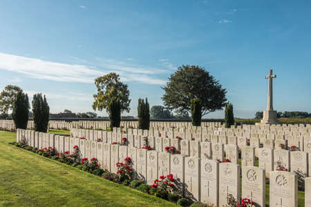 Proven, Flanders, Belgium - September 15, 2018: Overview of Mendinghem British war cemetery under blue morning sky. Green lawn, beige tomb stones and red roses with dark green trees sprinkled.のeditorial素材