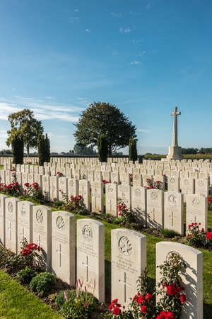 Proven, Flanders, Belgium - September 15, 2018: Overview of Mendinghem British war cemetery under blue morning sky. Green lawn, beige tomb stones and red roses with dark green trees sprinkled.のeditorial素材