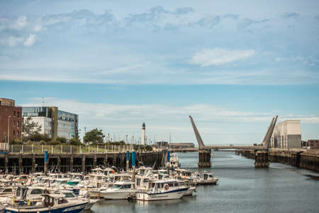 Dunkerque, France - September 16, 2018: The channel link to North Sea of old port in Dunkirk with motor yachts, bridge and buildings on side under light blue sky. Lighthouse on horizon.のeditorial素材