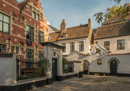 Kortrijk, Flanders, Belgium - September 17, 2018: Twilight falls on corner of the beguinage with white and red brick housing. Gray courtyard. Some green foliage.のeditorial素材